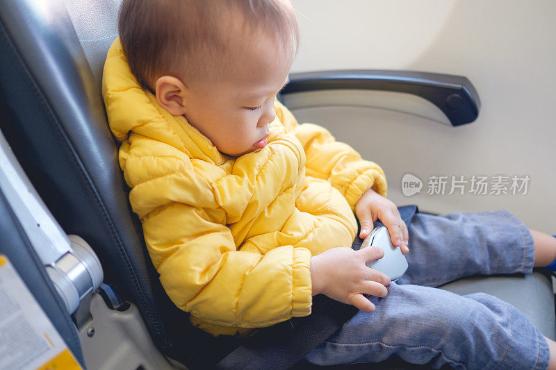 可爱的亚洲小男孩20个月/ 1岁的蹒跚学步的婴儿男孩在飞机座位上系好安全带